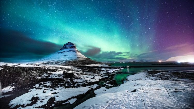 Solo traveler walking in front of an awesome Northern Lights in Mount Kirkjufell Iceland.